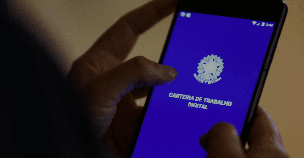 Mãos segurando celular. Tela do celular mostra a carteira de trabalho digital brasileira.