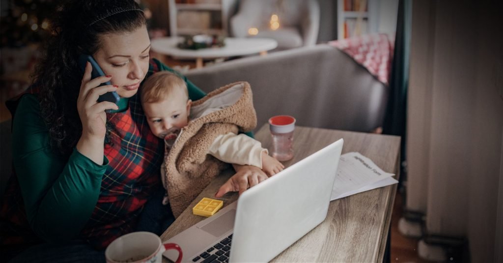 Mulher trabalhando no computador enquanto segura e cuida de seu filho