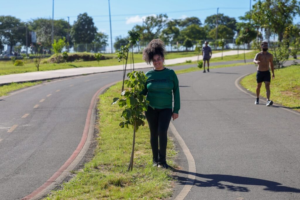 Larissa Brenda Cordeiro, presidente do Instituto Filhas da Terra, exibe muda de ipê plantada em parque urbano próximo a Sol Nascente. O calor agrava sua asma e fibromialgia